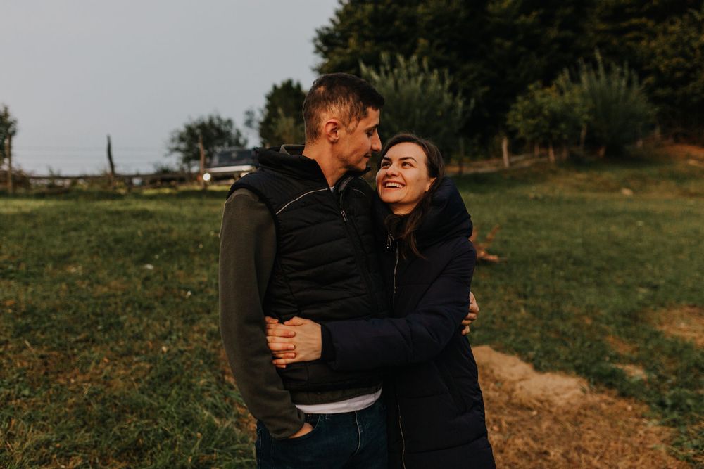 Happy couple hugging and laughing together in a green field at dusk.