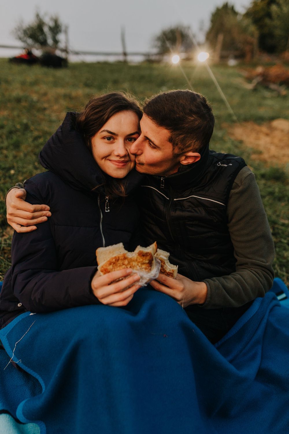 Romantic couple sharing sandwiches on a blue blanket at golden hour.