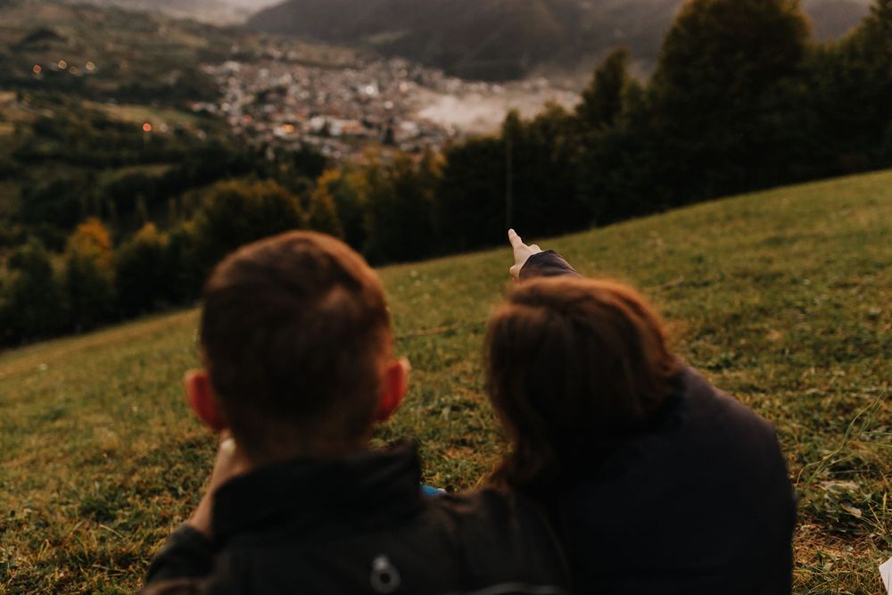 Couple sitting on hillside pointing at a misty mountain town below.