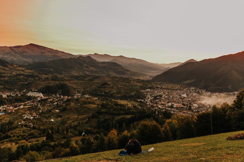 Panoramic sunset view of a mountain valley town with rolling green hills.