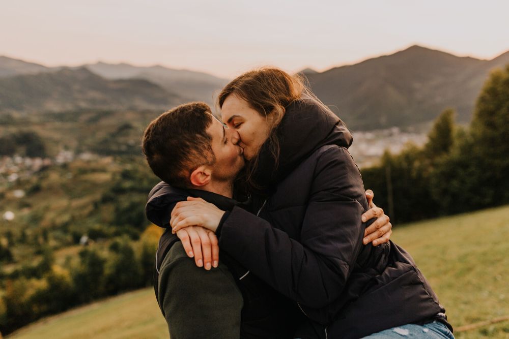 Couple sharing a romantic kiss on a hillside with mountain valley views.