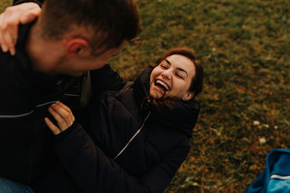 A joyful young woman laughs while lying on grass with her partner during an outdoor date.