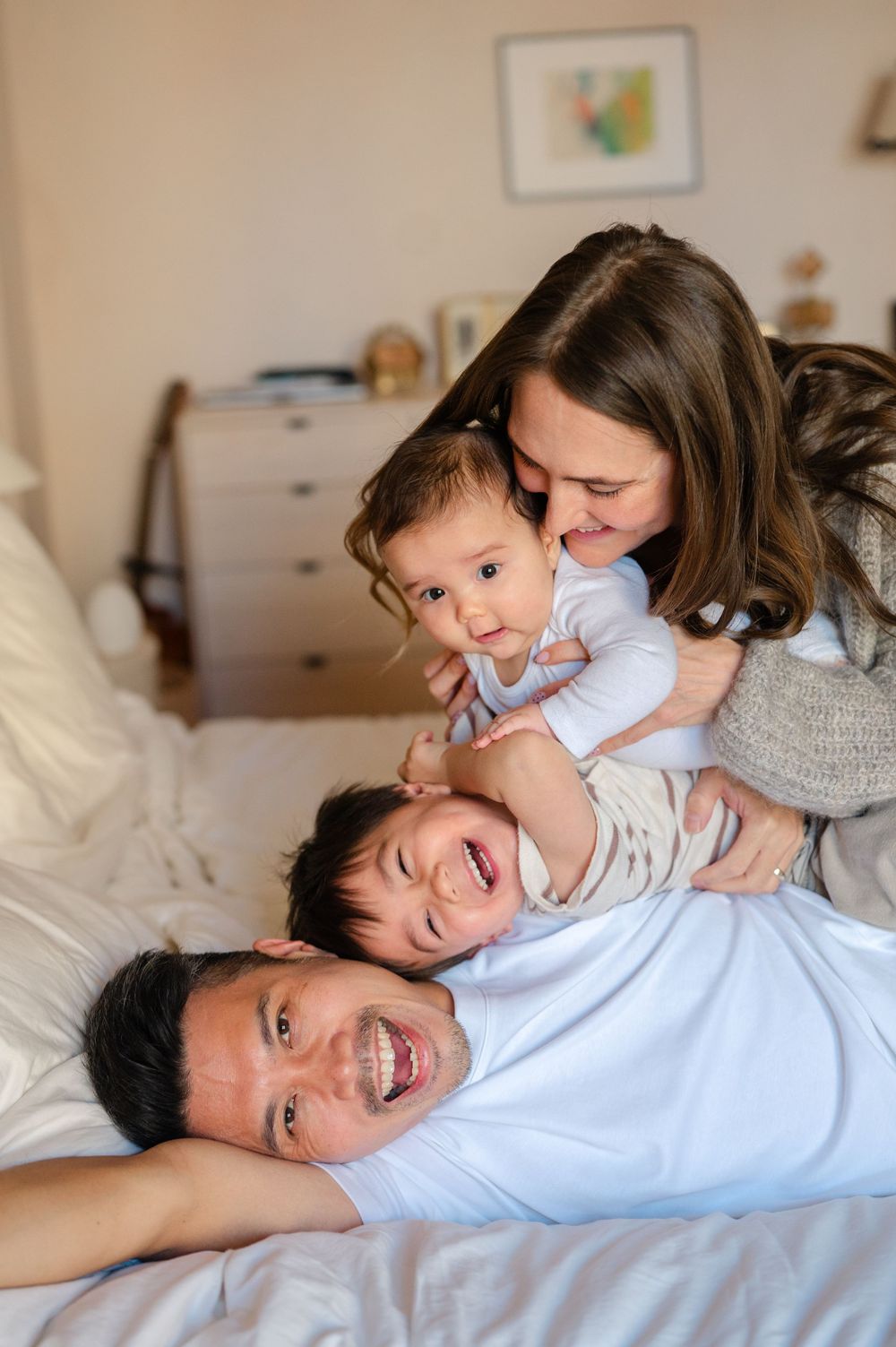 Joyful family of four playing together on a bed, with parents cuddling two young children.