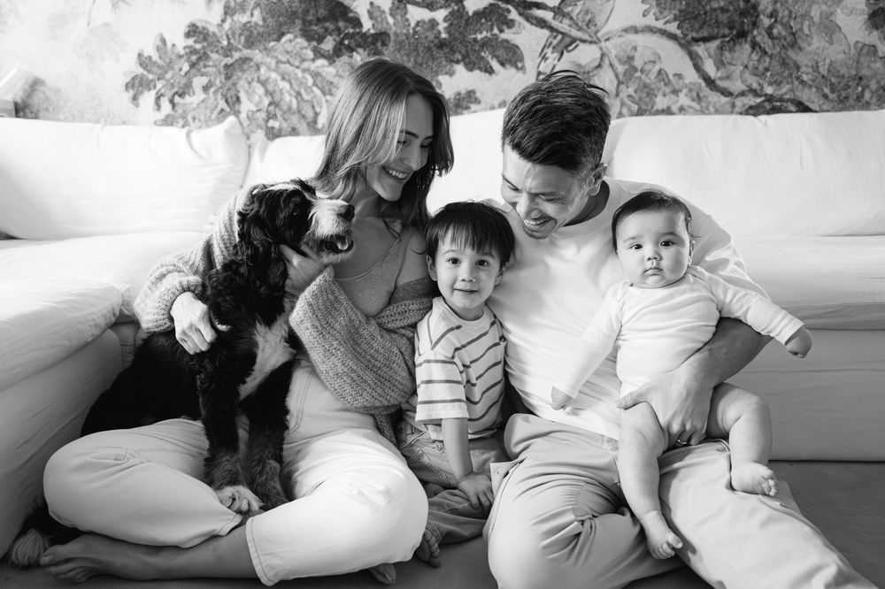 Black and white family portrait with parents, two young children, and a Bernedoodle dog on sofa.
