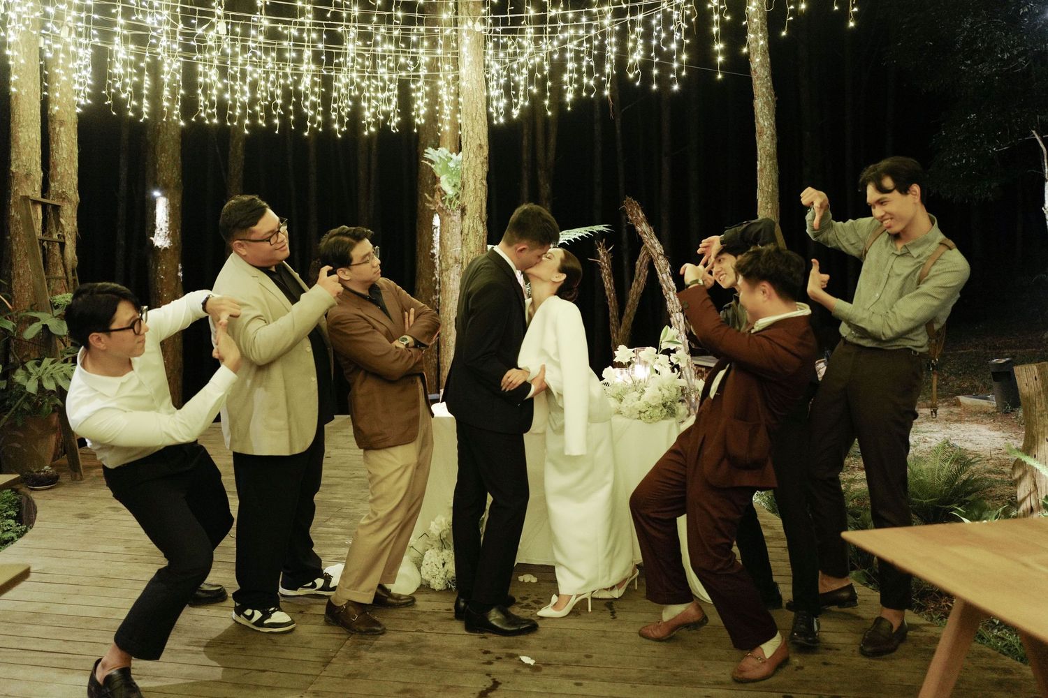 Wedding couple celebrates with guests dancing outdoors under string lights at a rustic venue.