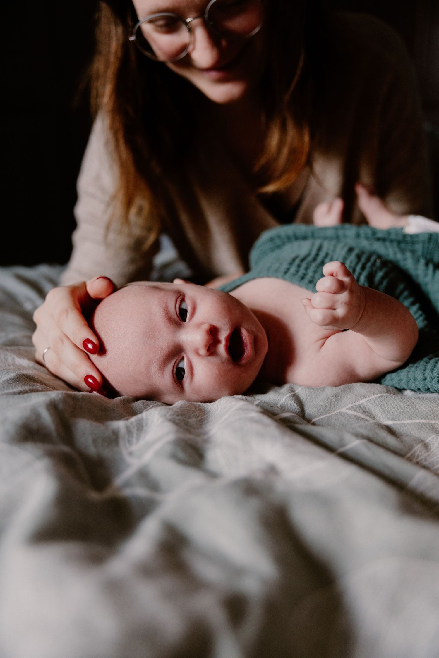 Smiling mother with red nails gently cradling her newborn baby's head on a bed.