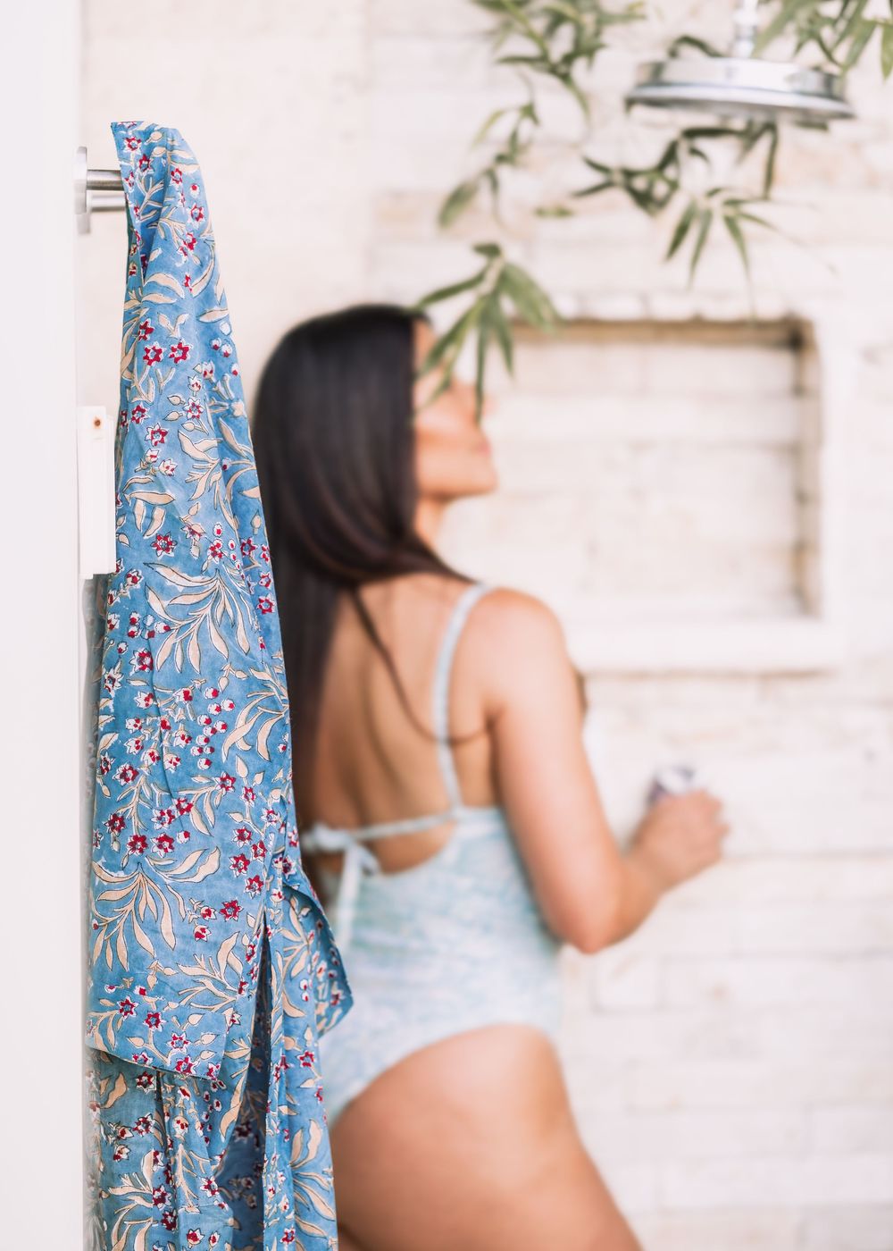 Blue floral kimono robe hanging on a door with a woman in a light blue bodysuit in background.