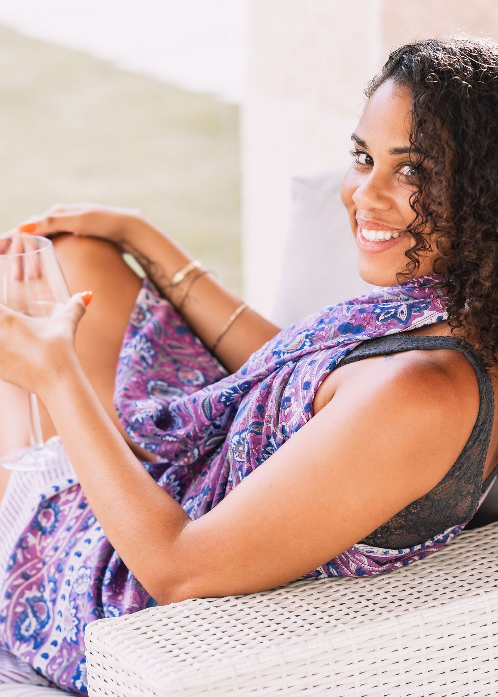 Smiling woman in purple paisley top relaxing on outdoor lounge chair.