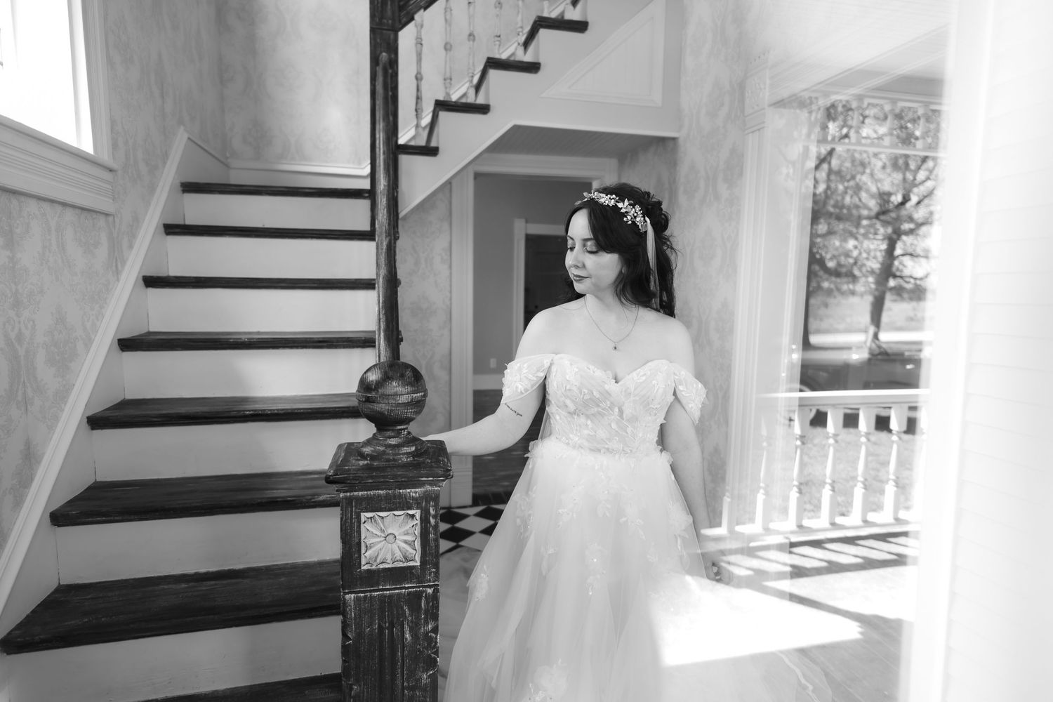Bride in white gown sitting on floral swing outdoors, holding bouquet, wearing flower crown, eyes closed, surrounded by green trees.