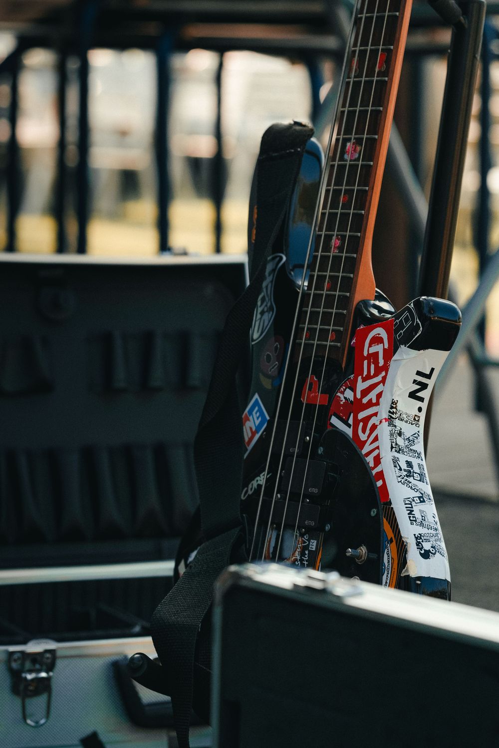 Bass guitar covered in stickers leaning against road case backstage at outdoor music venue.