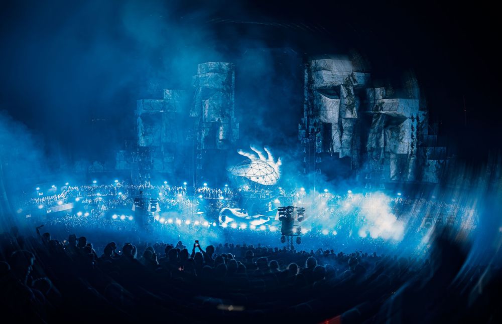Massive blue-lit concert stage with elaborate rock formation set design and crowd silhouettes.
