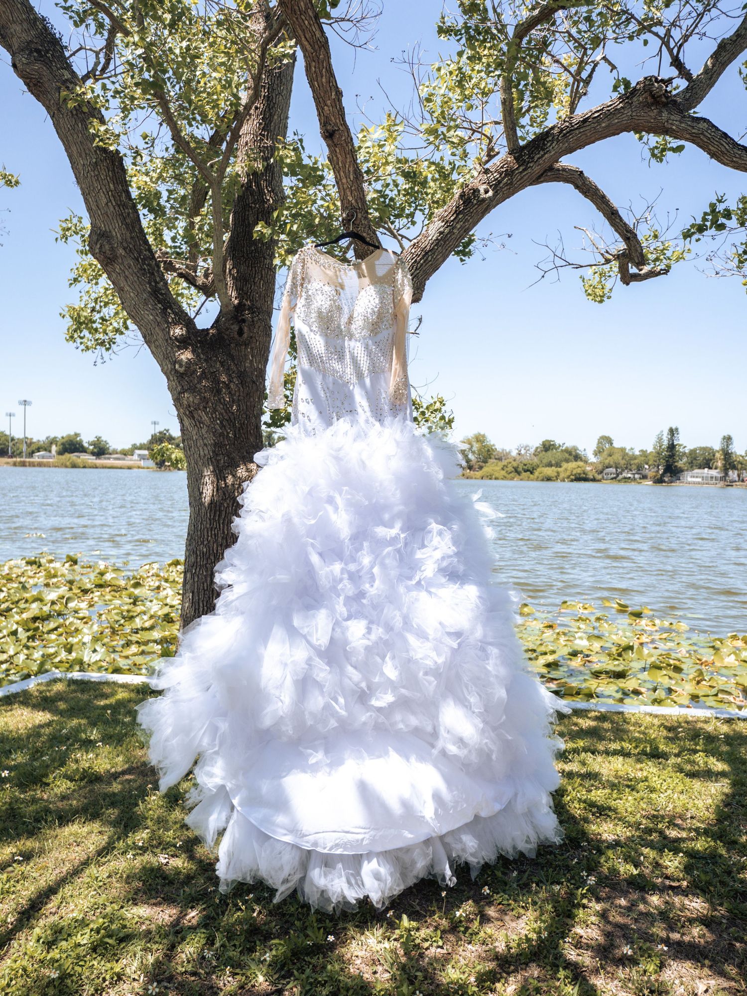 Bride in elegant white ballgown with flowing veil holds bouquet outdoors near palm trees on brick pathway.