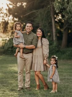 Family of four posing outdoors in neutral tones with two young daughters in a green park.