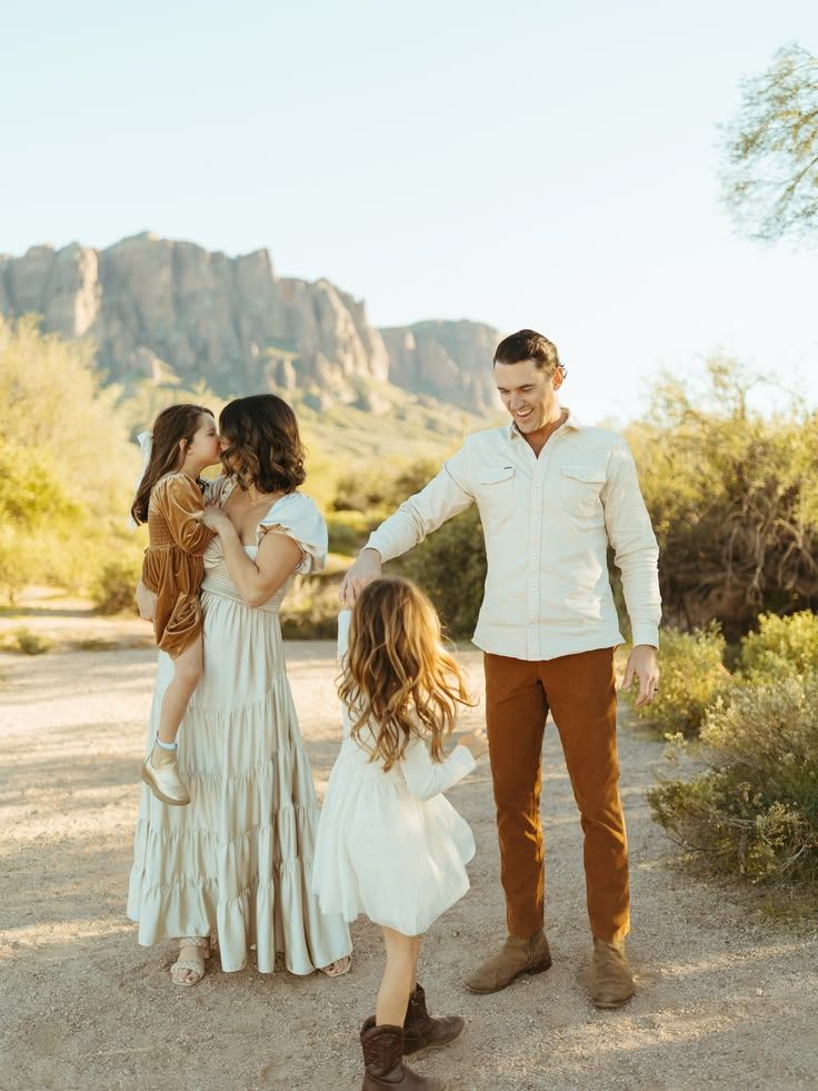 Family of four in desert landscape with mountains, wearing earth tones near Arizona cacti.