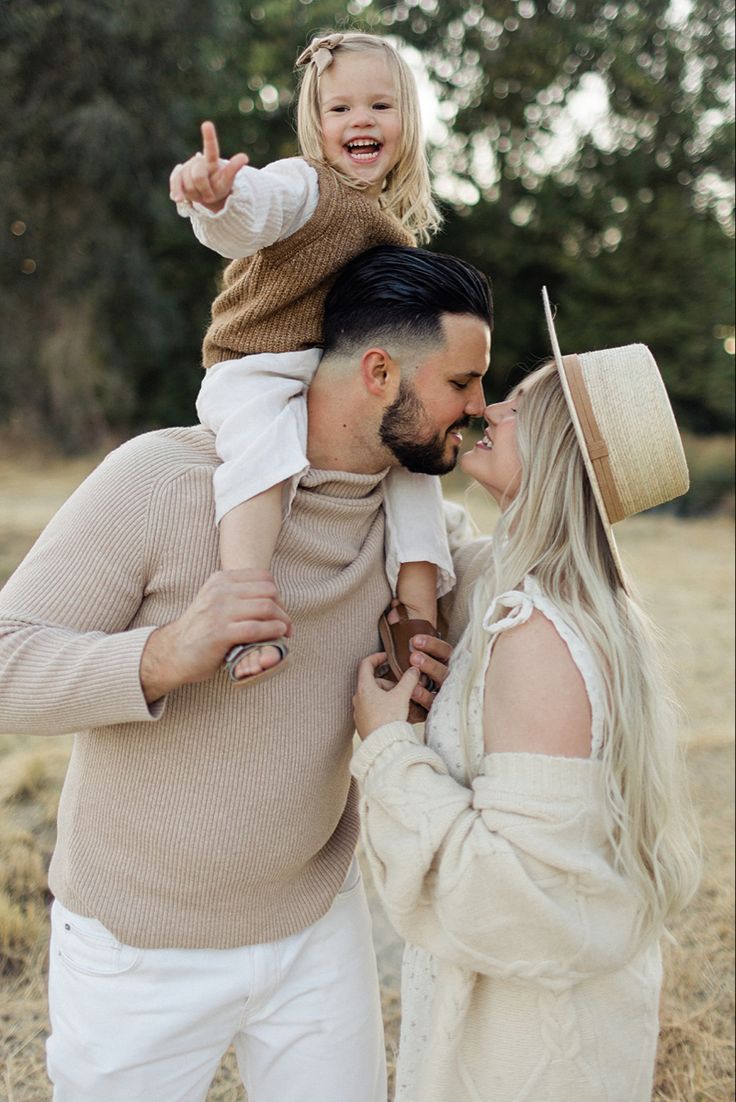 A loving family wearing neutral tones embraces and shares a joyful moment together in a sunlit outdoor setting.