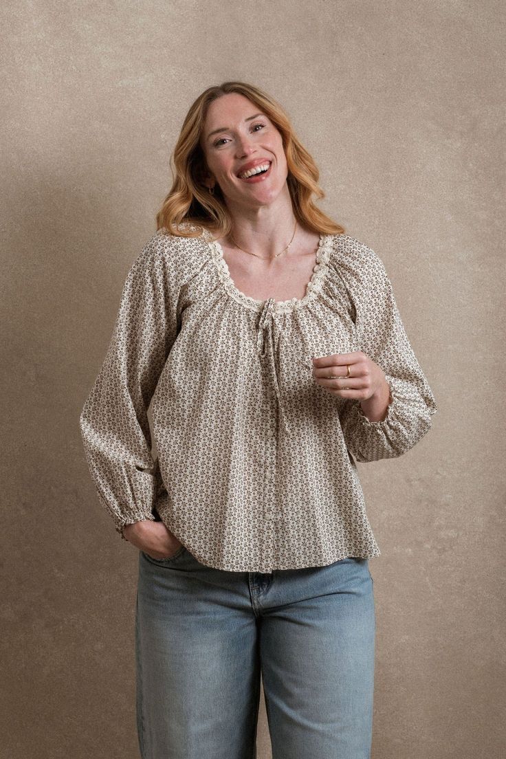 Woman smiling in a floral print peasant blouse with lace trim neckline and light blue jeans.