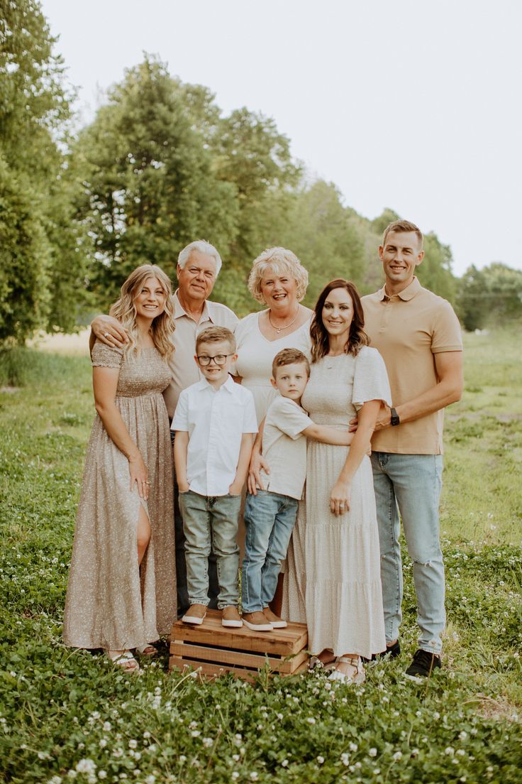 Multi-generational family portrait outdoors in a green meadow, featuring grandparents, parents, and two young boys.