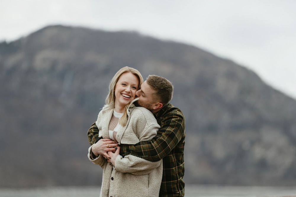 Happy couple embracing outdoors with a mountain and lake in the background.