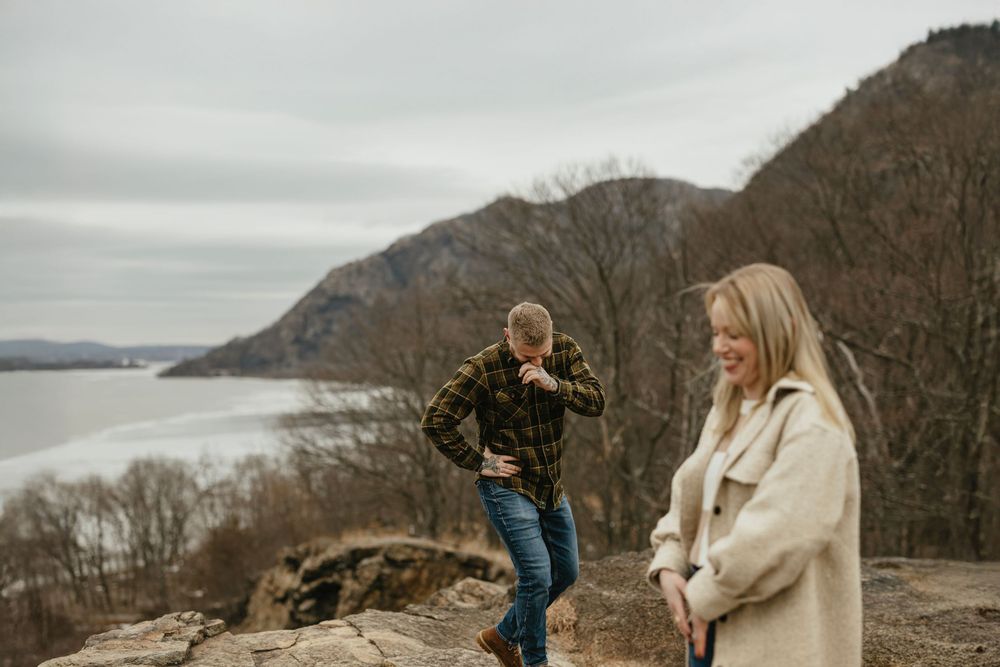 Couple standing on rocky overlook with river and mountain views on a cloudy day.