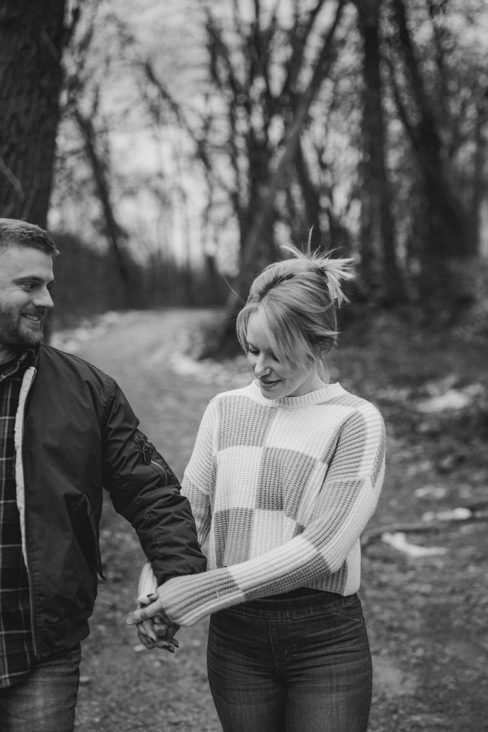Black and white photo of a couple holding hands while walking on a forest path.