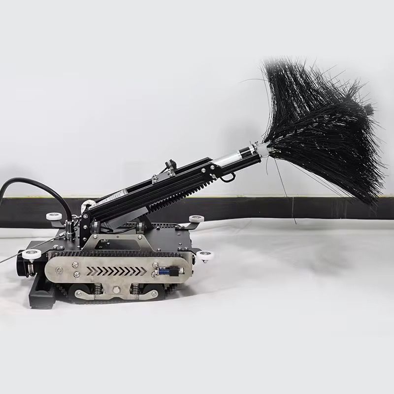 Robotic cleaning machine with articulated arm and black feather duster attachment on tracked base platform.