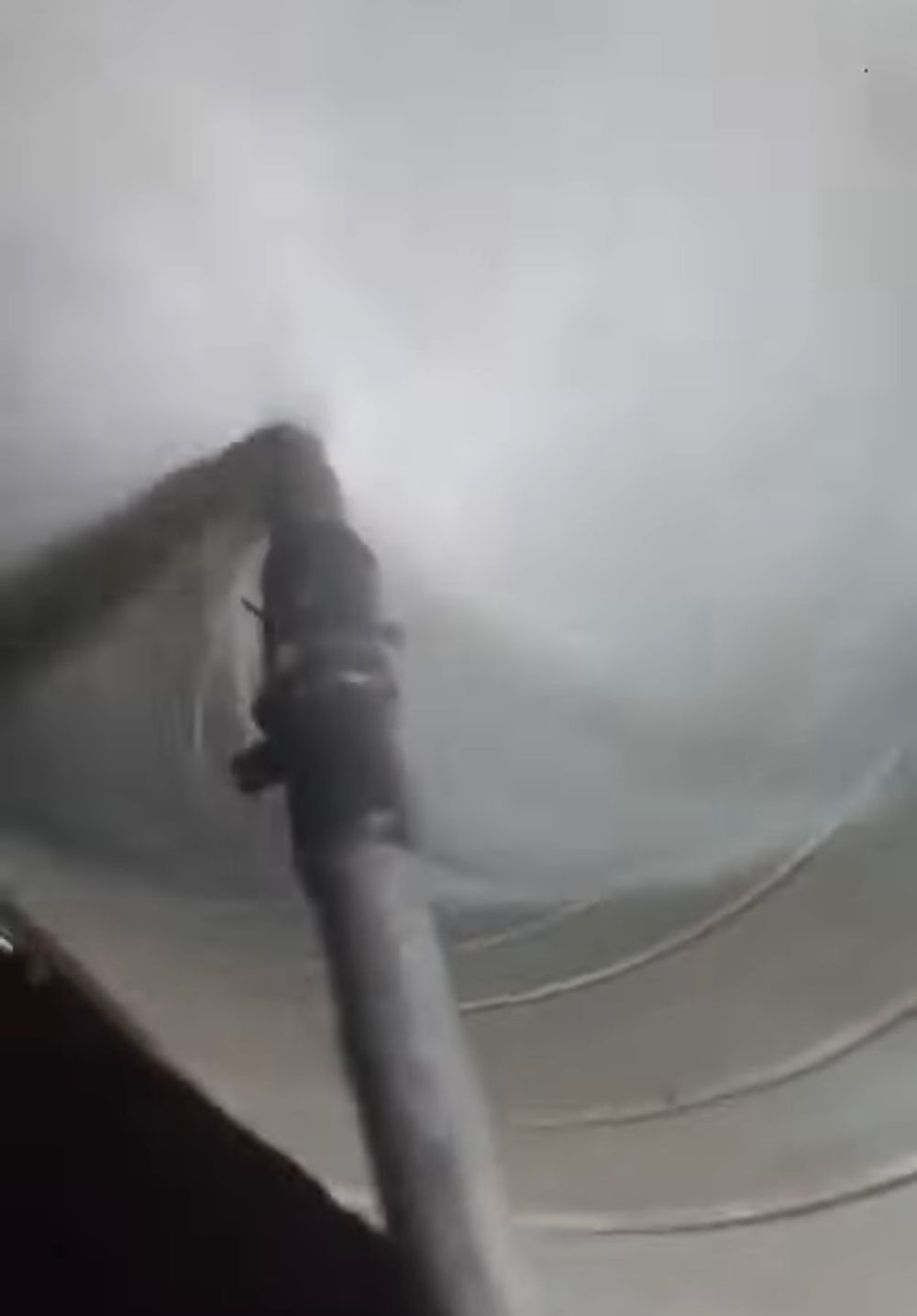 Close-up view of a metal pipe fitting attached to the interior wall of a white cylindrical tank.