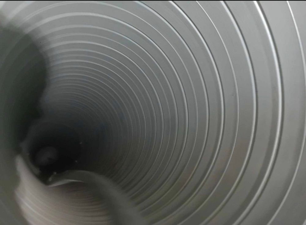 Close-up interior view of a spiral metal duct, showing circular ridges receding into darkness.