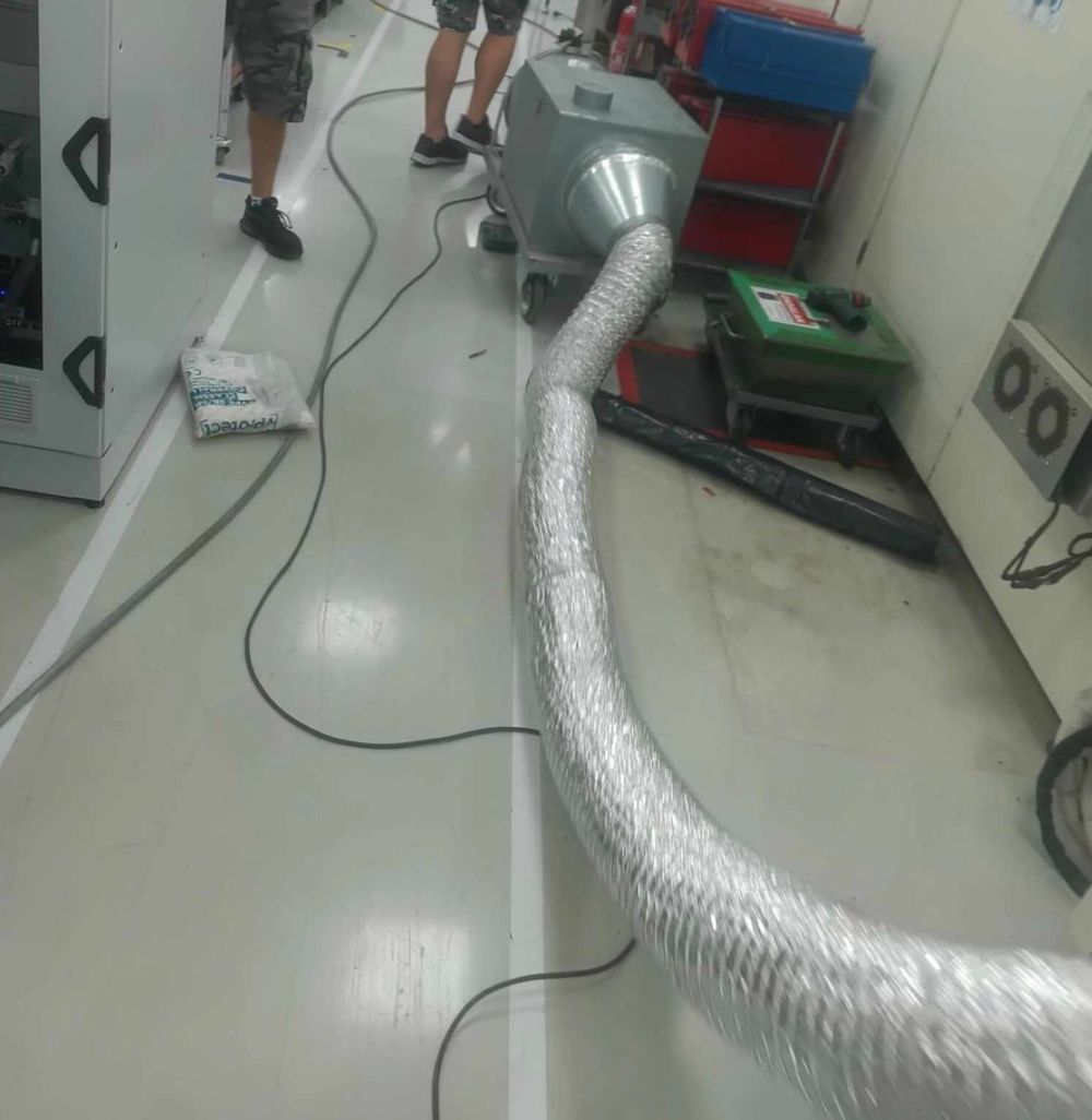 Industrial air duct hose connected to a green air mover machine on a white floor in a commercial facility.