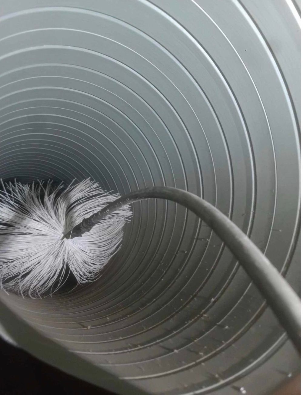 A dryer vent cleaning brush inside a round metal duct, removing lint and debris for improved airflow and safety.