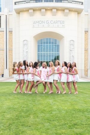 Group of young women in pink and white outfits posing cheerfully outside Amon G. Carter Stadium.
