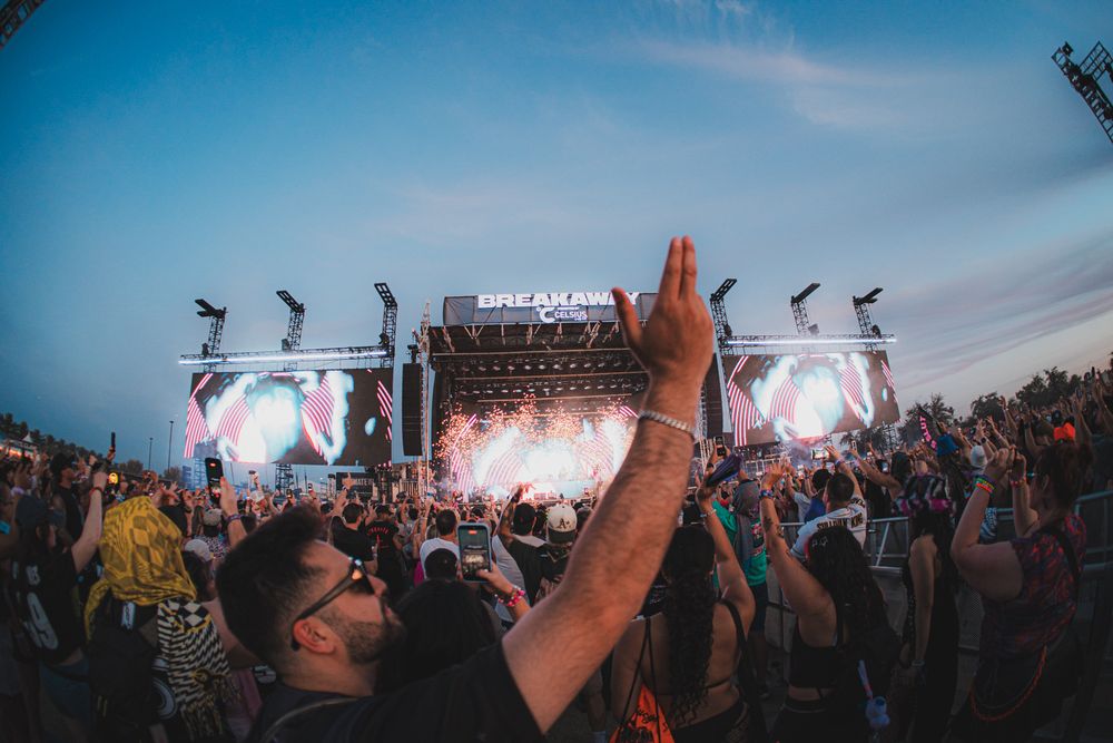 Crowd cheering at Breakaway Music Festival with colorful stage lights at dusk.