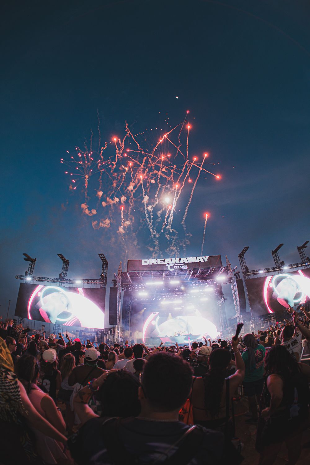 Crowd at Breakaway Music Festival enjoys fireworks exploding over the illuminated main stage at night.
