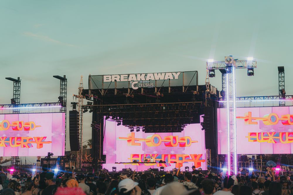 Breakaway Music Festival main stage lit with pink and yellow lights at dusk with a large crowd.