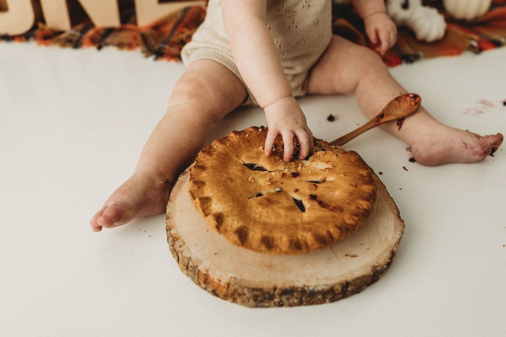 Baby reaching into a homemade pie on a wooden slice during a first birthday smash photo session.