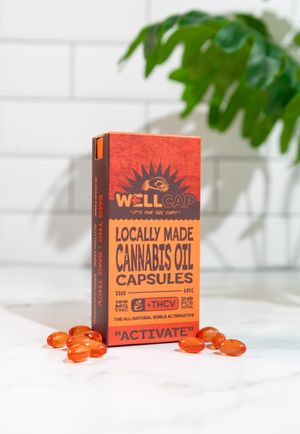 Orange cannabis oil capsules displayed with Well Cap product box and green plant in background.