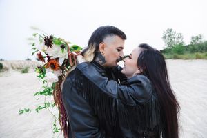 A couple in black attire share romantic moments on a beach during a photo session.