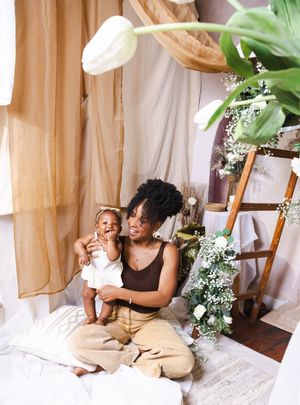 A person relaxes in a cozy indoor tent fort decorated with white sheets, plants and soft lighting.