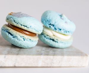 Light blue macarons with cream filling arranged in a row on a white marble surface.