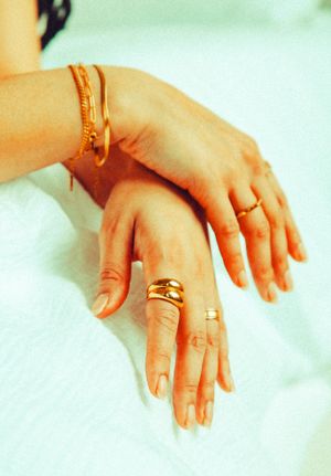 Woman's hands adorned with gold rings and bracelet resting on white fabric.
