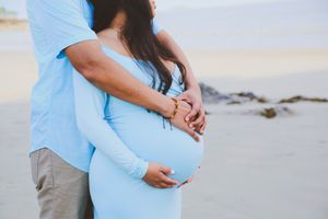 A couple embracing on a sandy beach during golden hour with soft lighting.