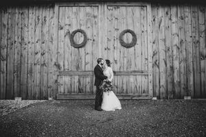 A couple shares a romantic moment in black and white against a rustic wooden barn wall.