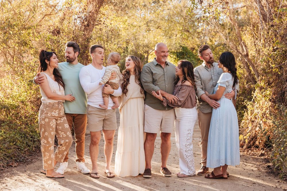 Large extended family group portrait outdoors on a sunny dirt path surrounded by golden foliage.