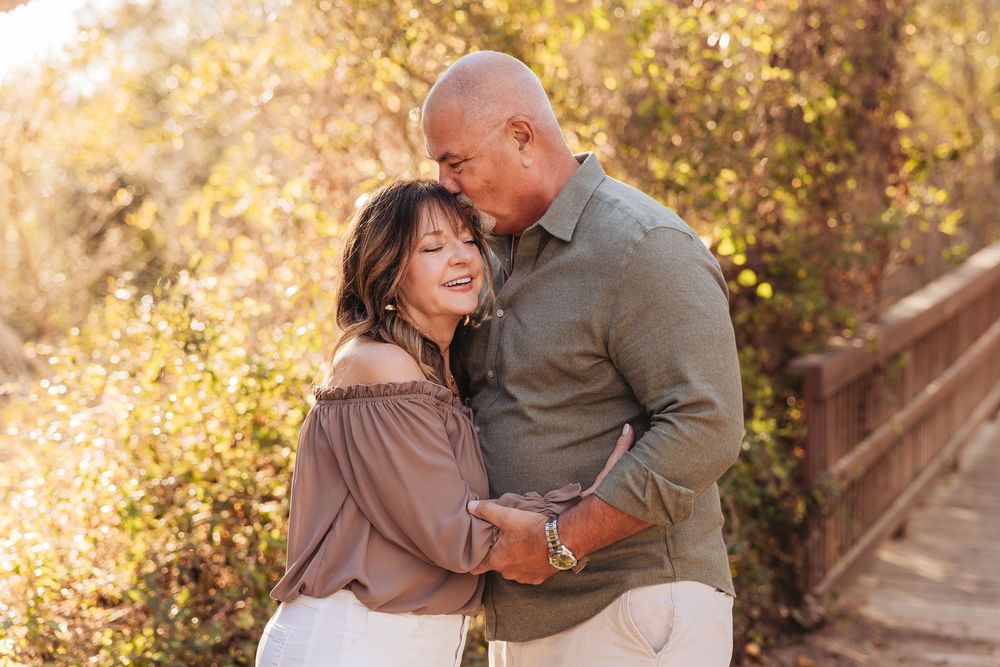 Romantic couple embracing and smiling outdoors in warm golden light near wooden bridge.