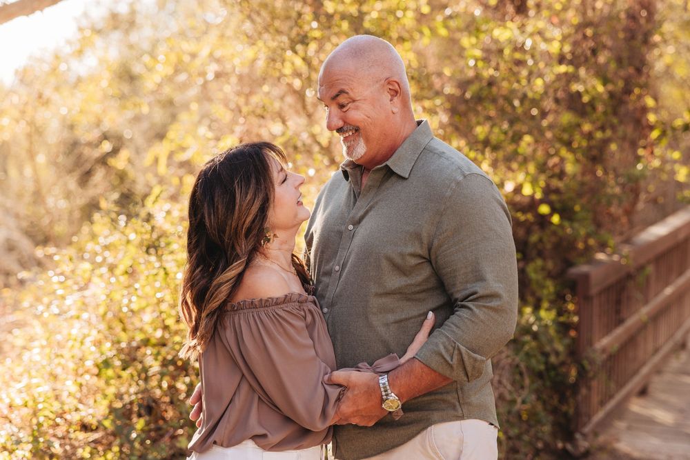 Couple sharing a romantic moment outdoors in golden sunlight, smiling at each other among autumn foliage.