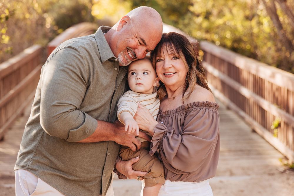 Happy family portrait of parents smiling with baby on a wooden bridge outdoors.