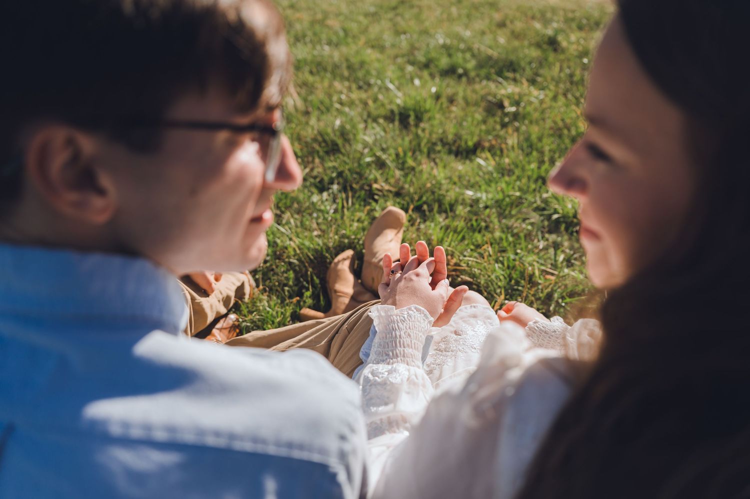 Couple lying on green grass field, smiling and enjoying a sunny day together outdoors.