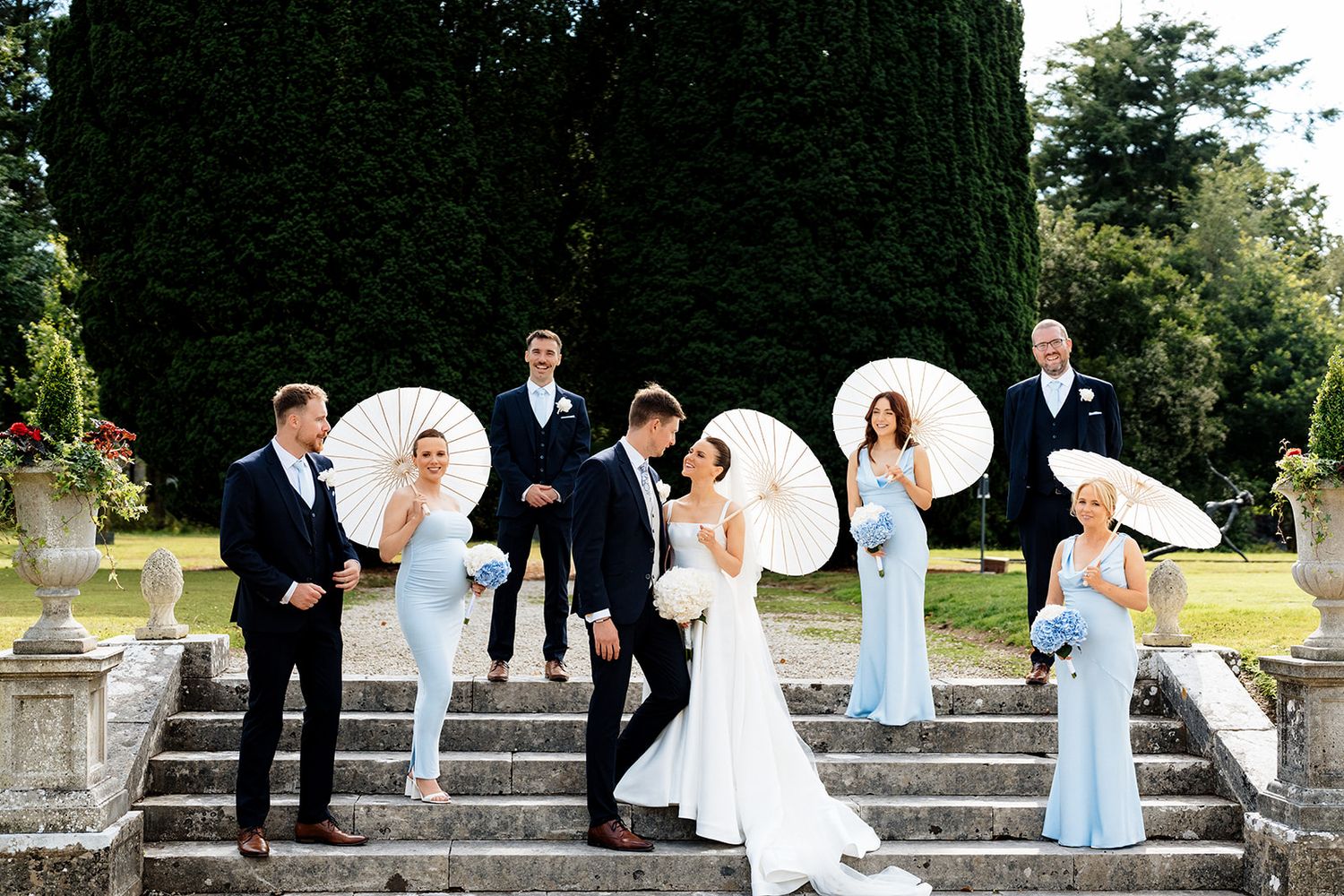 A creative wedding photo sequence shows couples posing with white umbrellas on outdoor stone steps in formal attire.