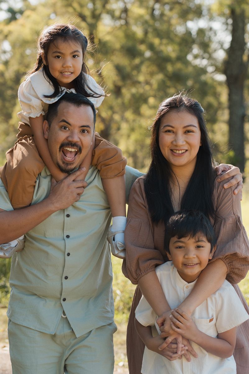 Happy family posing outdoors, father carrying daughter on shoulders with mother and son smiling in sunny rouse hill park family photoshoot