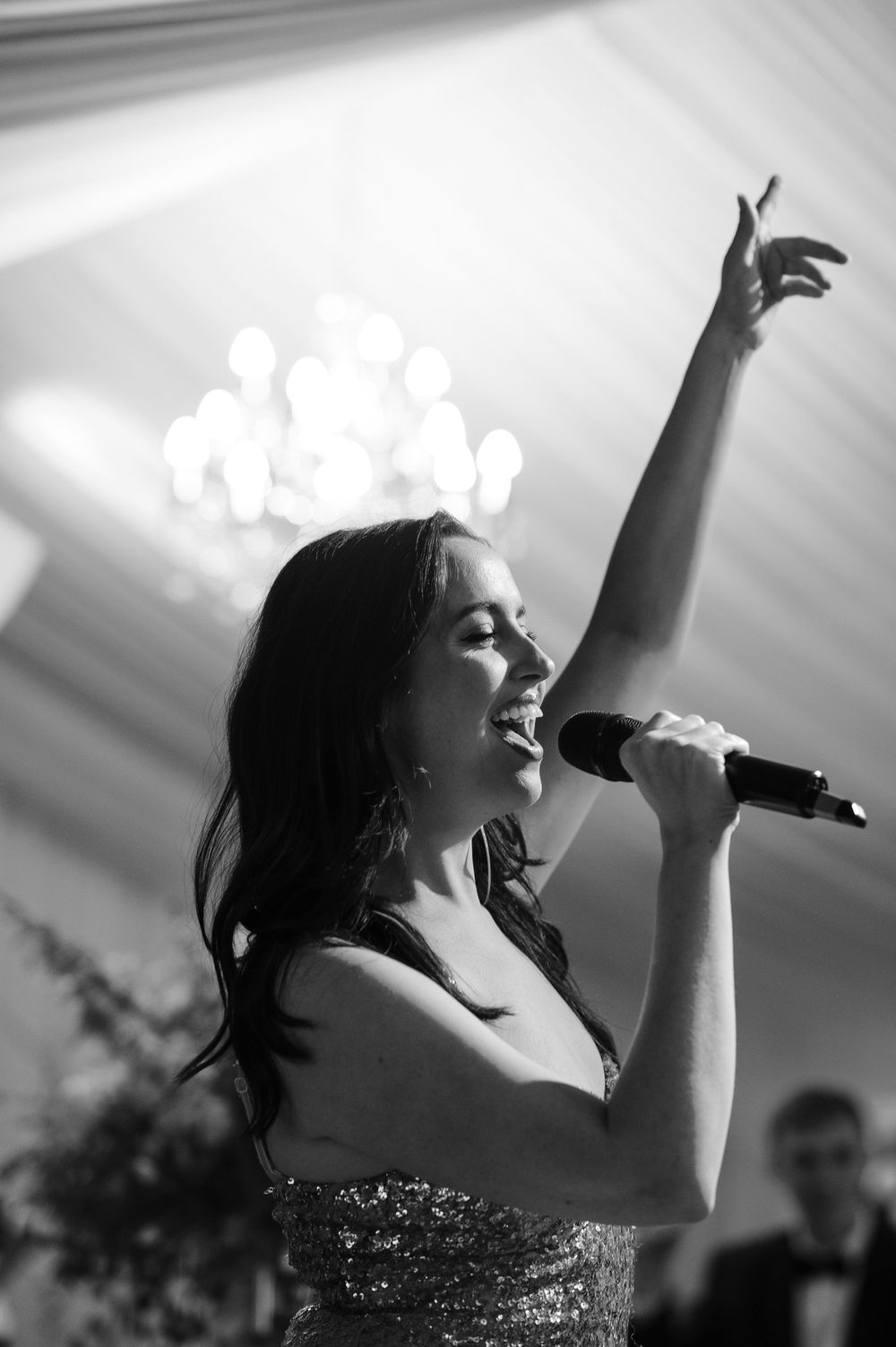 Black and white photo of a woman singing passionately into a microphone with one arm raised at a formal event.