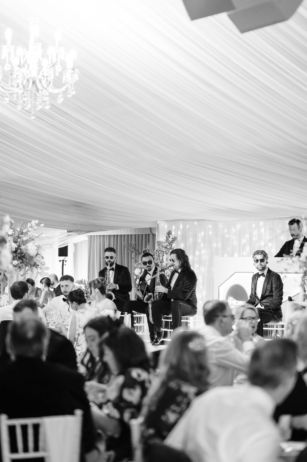 Black and white photo of a live band performing saxophones at an elegant wedding reception under draped ceiling.